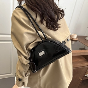 Minimalist black patent leather bowling shoulder bag with silver plaque shown on model