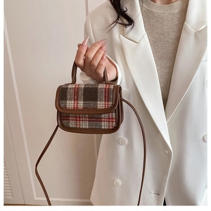 Detail of plaid wool and brown leather mini crossbody bag held against white blazer