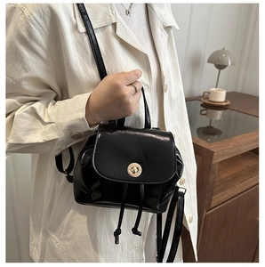 Glossy black mini backpack with gold twist-lock and drawstring detail in cozy setting