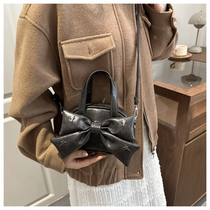 Détail du sac seau à nœud noir avec rivets en étoile porté avec une tenue d'automne chic
