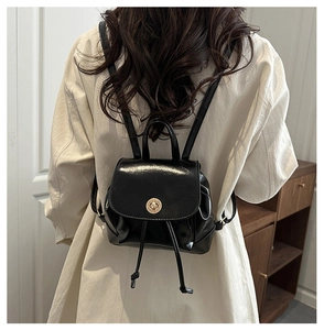 Detail of black patent leather mini backpack featuring a gold-tone twist lock closure