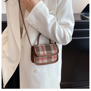 Detailed close-up of mini plaid crossbody bag with brown leather trim on white blazer background
