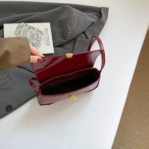 Sac baguette chic en cuir verni bordeaux avec fermoir doré posé sur un blazer gris