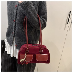 Detail of burgundy shoulder bag with front flap pockets and cherry metal charm