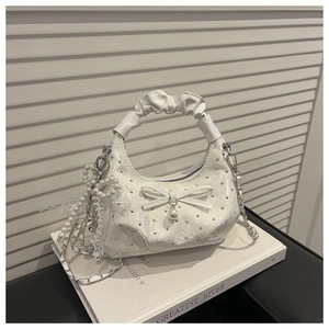 Detailed macro of white rhinestone handbag featuring pearl bow and silver chain strap