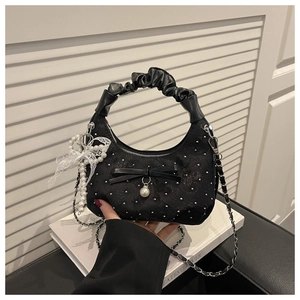 Elegant black ruched chain bag with diamond bow and pearl charm shown held by hand