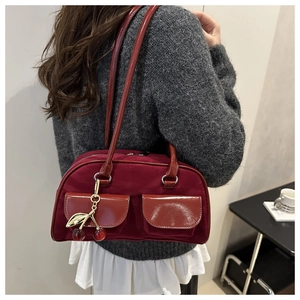 Detail of burgundy suede shoulder bag with dual patent pockets and cherry charm on a model
