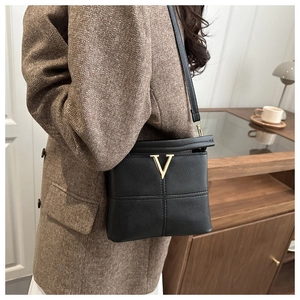 Detail of black pebbled leather crossbody bag with gold V-shape logo and quilted stitching