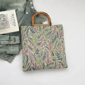 Floral embroidered canvas tote bag with natural bamboo handles on a minimalist background