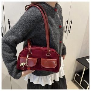 Detail of dark red faux suede shoulder bag featuring side pockets and cherry charm