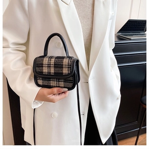 Detail of mini plaid handbag with black leather trim and strap held by a model