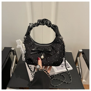 Detail of black pleated handbag featuring bow, pearl pendant and lace charms