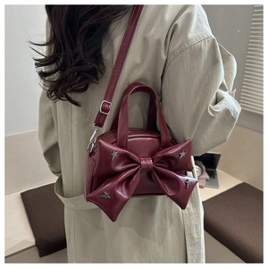 Détail du sac seau bordeaux avec grand nœud et étoiles argentées sur un trench-coat beige