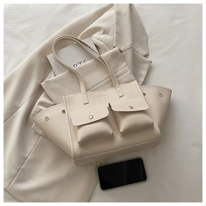 Détail du sac cabas beige montrant le cuir grainé et les poches avant à pressions dorées