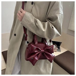 Dettaglio borsa a tracolla rosso vino con grande fiocco e stelle argentate su una modella