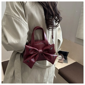 Détail du sac à main bordeaux avec grand nœud et clous étoiles argentés sur manteau beige