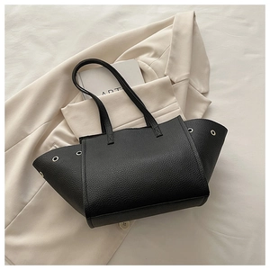 Détail d'un sac cabas noir grainé avec œillets métalliques sur un blazer beige chic