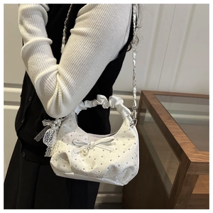 Detail of white satin shoulder bag featuring rhinestone bows, pearls and lace ribbons