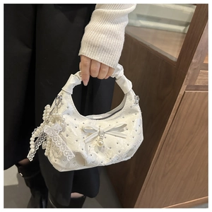 Close-up of white pleated handbag with rhinestone accents, pearl chain and lace bow