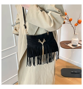 Gros plan du sac bandoulière en daim noir avec pendentif cerf doré et pompons