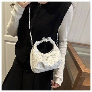 Detail of white lace shoulder bag with rhinestone bow and pleated handle worn by model