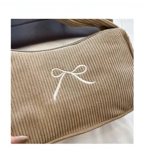 Detailed macro view of khaki corduroy fabric with white embroidered bow detail on the bag