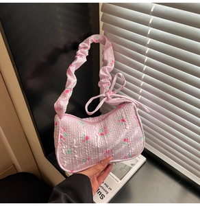 Detailed close-up of pink floral embroidery and pleated ruffle shoulder strap on the hobo bag