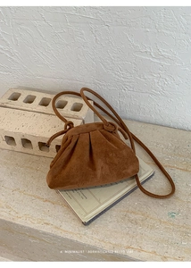 Detail of a brown suede pouch bag with elegant pleats on a vintage book backdrop