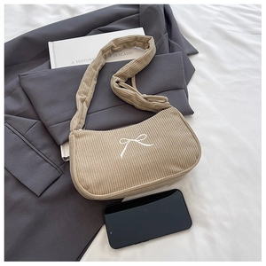 Detail of beige corduroy underarm bag featuring white bow embroidery and zip closure