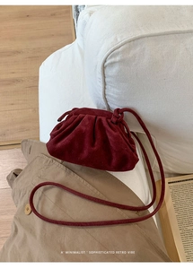 Detailed retro burgundy suede handbag with gathered pleats on a white sofa scene