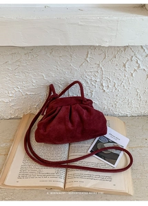 Close-up of wine red pleated cloud bag with suede texture on a vintage book