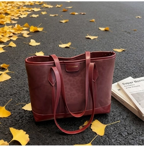 Détail du sac cabas bordeaux texturé avec plaque de marque sur fond de feuilles d'automne