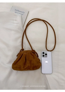 Top view of caramel brown pleated cloud bag on white fabric with a phone for size scale