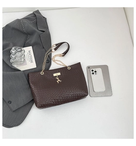 Flat lay of brown woven tote bag with gold deer charm and chain strap on minimalist background