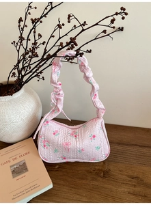 Detailed close-up of a pink floral underarm bag with ruffled textures on a wooden table