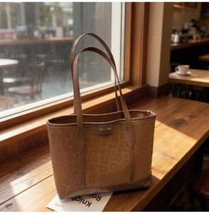 Détail du sac cabas marron foncé avec motif léopard posé sur une table en bois