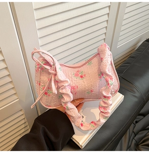 Detailed view of pink quilted handbag featuring red rose patterns and side bow accents