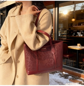Detail of burgundy leopard print tote bag with metal brand plate in sunny cafe setting