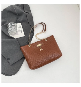 Detail of brown woven bucket bag with gold chain strap and deer pendant on white desk