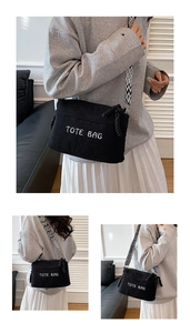 Detail of black corduroy crossbody bag featuring white TOTE BAG embroidery and strap