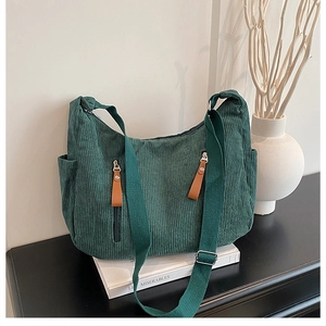 Detail of dark green corduroy shoulder bag showing dual front zip pockets and texture