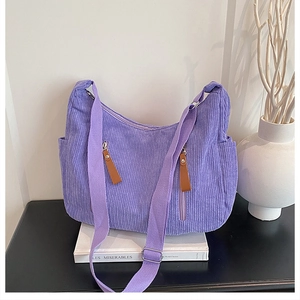 Detail of purple corduroy crossbody bag featuring dual vertical zippers and wide strap
