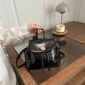 Glossy black mini backpack with gold twist lock and drawstring on wooden table