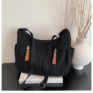 Detail of black corduroy tote bag showing front zipper pockets with brown leather pulls