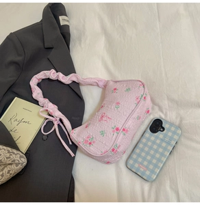 Detail of pink floral underarm bag featuring rose patterns and ruched handle texture