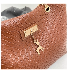 Detail of brown woven faux leather tote with golden clasp and deer charm accessory