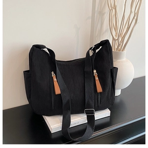 Detail of black corduroy dumpling bag featuring dual vertical zippers and brown pull tabs