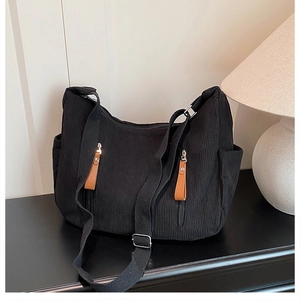 Detail of black corduroy shoulder bag with brown leather zipper pulls and front pockets
