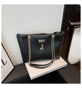 Detail of black woven bucket bag with gold chain strap and deer charm on white prop