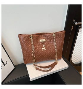 Detail of brown woven bucket bag with gold deer pendant and chain strap on white books